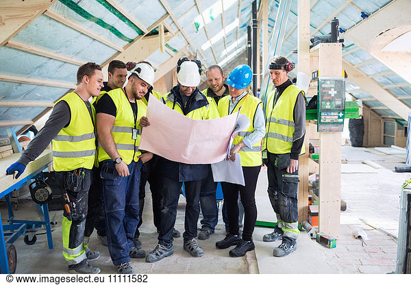 Manager standing with manual workers while reading blue prints at construction site