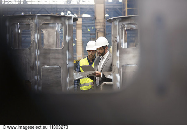 Manager und Stahlarbeiter mit Klemmbrettbesprechung in der Fabrik
