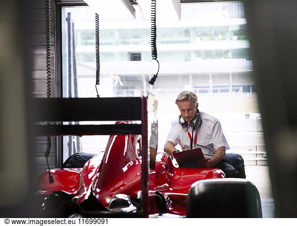 Manager with clipboard examining formula one race car in repair garage