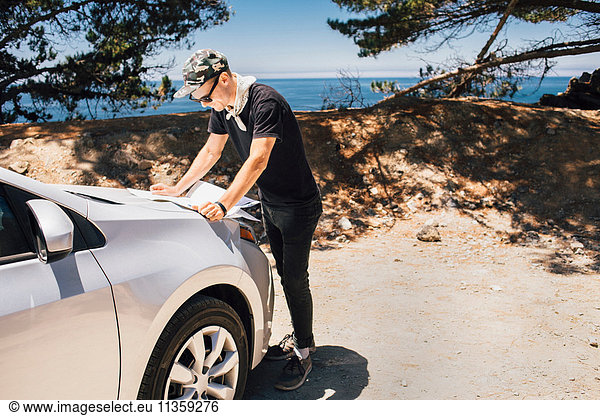Mann auf Autoreise liest Karte auf der Motorhaube eines Autos  Big Sur  Kalifornien  USA