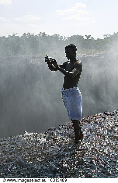 Mann auf dem Sims der Victoriafälle stehend  fotografiert  Sambia.