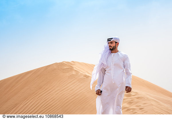 Mann aus dem Nahen Osten trägt traditionelle Kleidung auf Wüstendüne  Dubai  Vereinigte Arabische Emirate