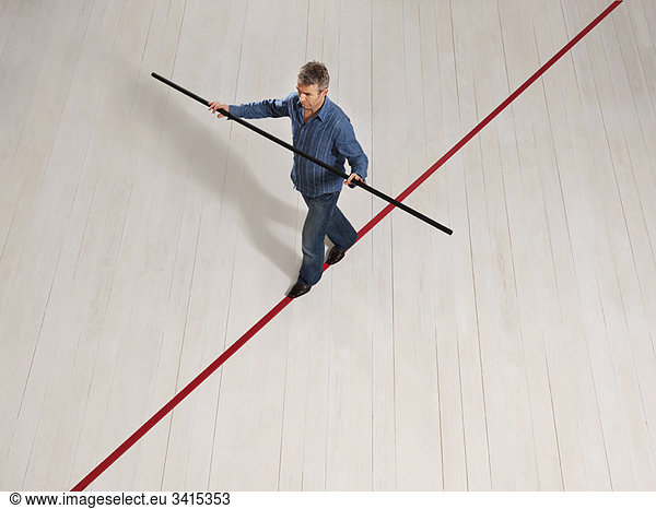 Mann balanciert auf dünner roter Linie mit Mast