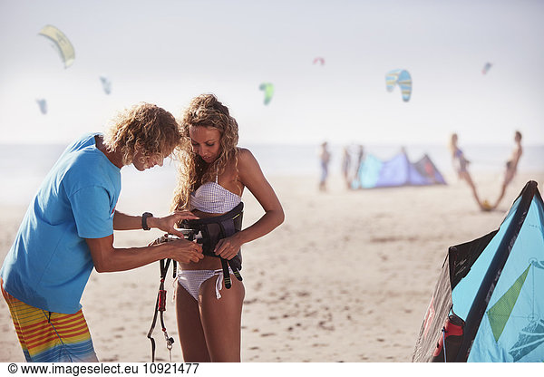 Mann befestigt Kiteboarding Sicherheitsgurt an Frau am sonnigen Strand