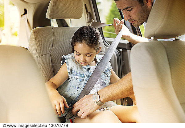 Mann befestigt Sicherheitsgurt für Tochter im Auto
