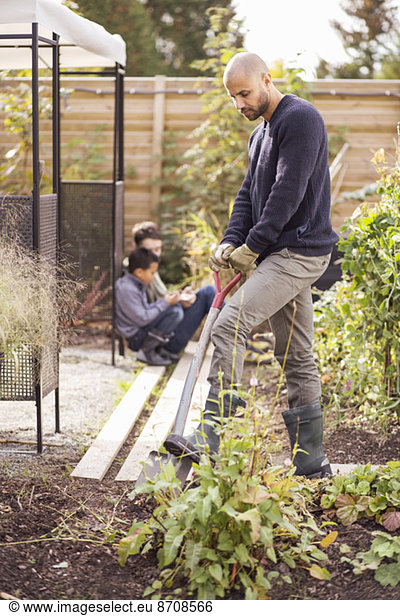 Mann beim Graben im Garten mit Kindern im Hintergrund