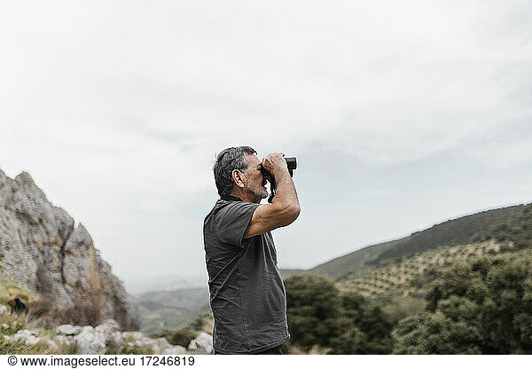 Mann betrachtet die Aussicht durch ein Fernglas auf einem Berg
