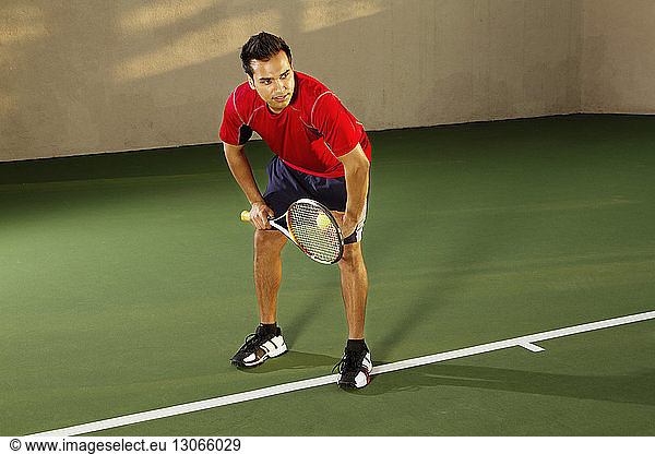 Mann beugt sich beim Tennisspielen auf dem Platz