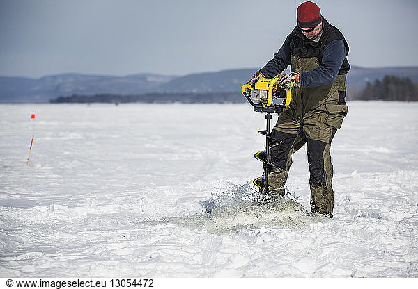 Mann bohrt gefrorenen See mit Ausrüstung