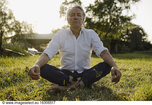 Mann übt Yoga  während er im Lotussitz im Hof sitzt