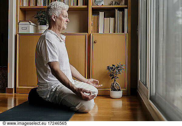 Mann übt Yoga  während er zu Hause im Lotussitz sitzt