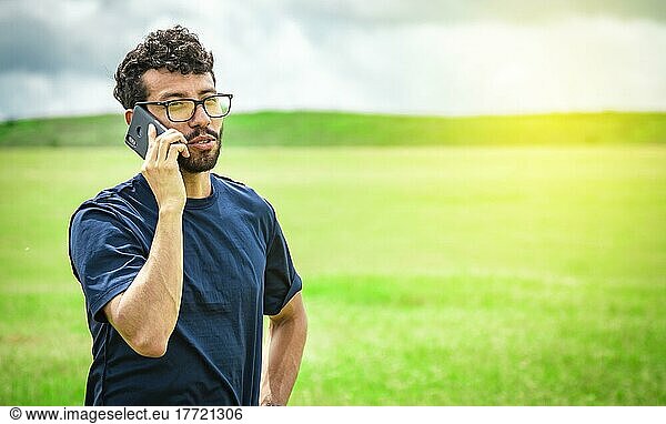 Mann  der auf dem Feld telefoniert  Mann auf einer Straße  der telefoniert  Person mit Handy auf dem Feld  die telefoniert  junge Person  die auf einem Feld telefoniert