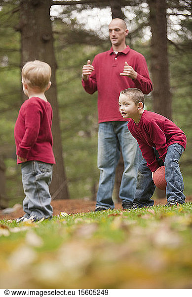 Mann  der das Wort Play in amerikanischer Gebärdensprache gebärdet  während er mit seinen Söhnen in einem Park spielt