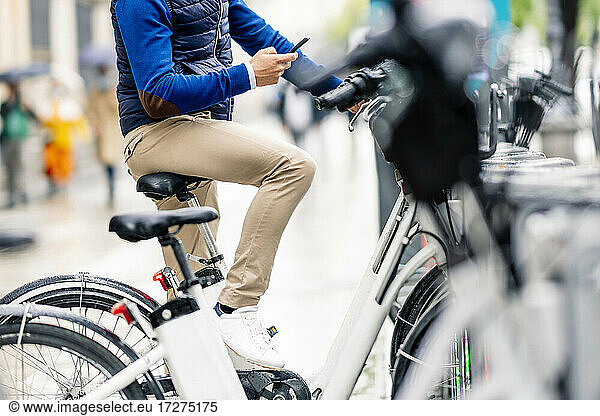 Mann  der ein Smartphone benutzt  sitzt auf einem Elektrofahrrad an einer Parkstation während des Coronavirus