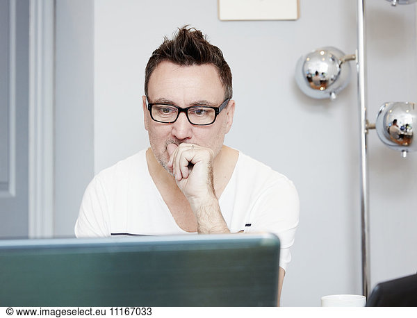 Mann  der mit einem Laptop an einem Schreibtisch in einem Büro sitzt.