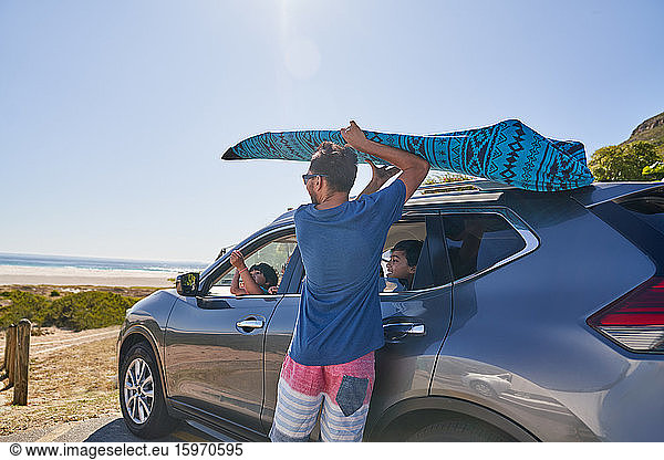 Mann entfernt Surfbrett vom Autodach auf einem Parkplatz am Strand