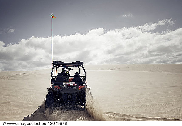 Mann fährt Golfwagen auf Sand in der Wüste vor bewölktem Himmel