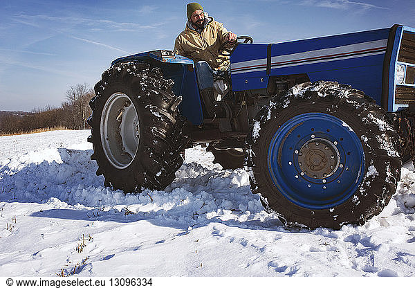 Mann fährt Schneepflug auf schneebedecktem Feld