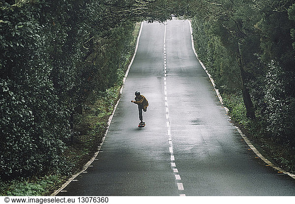 Mann fährt Skateboard auf der Straße inmitten des Waldes im Garajonay-Nationalpark