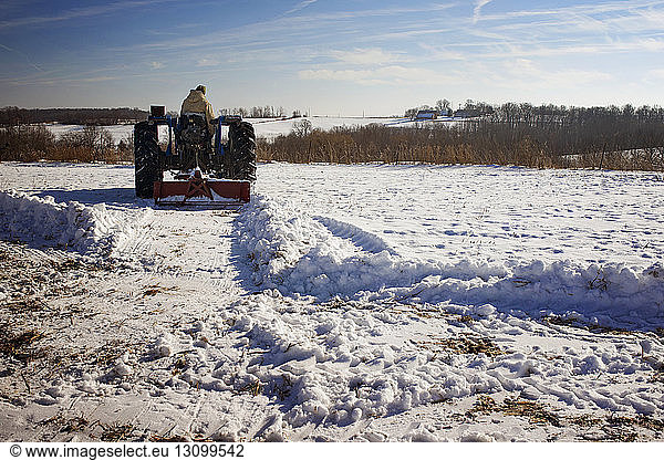 Mann fährt Traktor auf schneebedecktem Feld gegen den Himmel