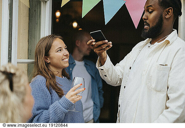 Mann fotografiert Freundin mit Weinglas während einer Dinnerparty im Café