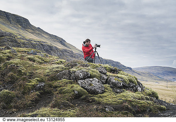 Mann fotografiert  während er auf einem Hügel vor bewölktem Himmel steht
