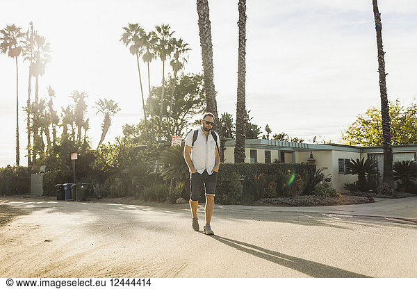 Mann geht mit einem Rucksack auf einer Wohnstraße in einem tropischen Klima; Long Beach  Kalifornien  Vereinigte Staaten von Amerika