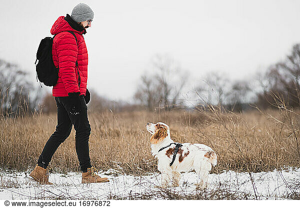 Mann geht mit Hund im Freien in winterlicher Natur spazieren