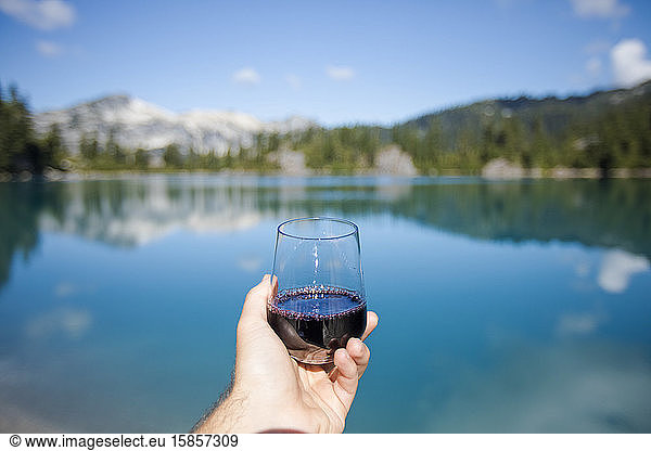 Mann hält Glas oder Rotwein am See.