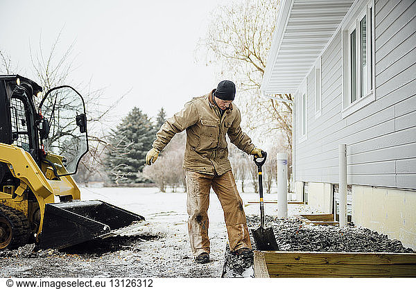 Mann hält im Winter im Hinterhof arbeitende Schaufel gegen den Himmel