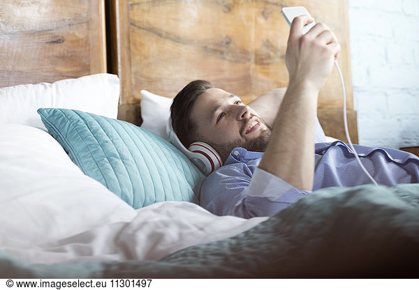 Mann hört Musik mit Kopfhörer und mp3-Player auf dem Bett liegend