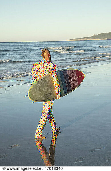 Mann im Anzug trägt Surfbrett beim Strandspaziergang