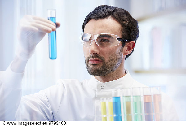 Mann im Labor beim Betrachten von Fläschchen mit blauer Flüssigkeit