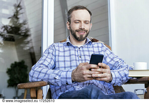 Mann in Freizeitkleidung benutzt Smartphone auf Balkon