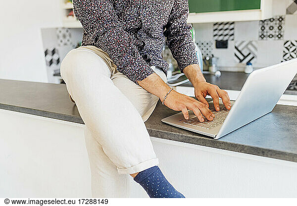 Mann in Freizeitkleidung mit Laptop auf Kücheninsel zu Hause