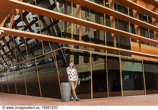Mann in Freizeitkleidung steht vor Bürogebäude  während er mobil ist