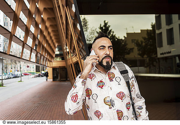 Mann in Freizeitkleidung steht vor Bürogebäude  während er mobil ist