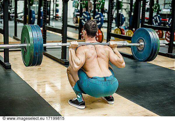 Mann in hockender Position beim Gewichtheben im Fitnessstudio