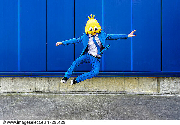 Mann in leuchtend blauem Anzug und Vogelmaske springt gegen eine blaue Wand