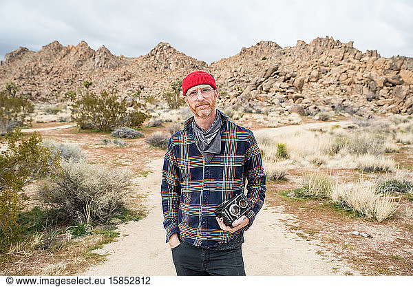 Mann in Mütze mit Bart und Brille an weit entfernten Steinhaufen in der Wüste