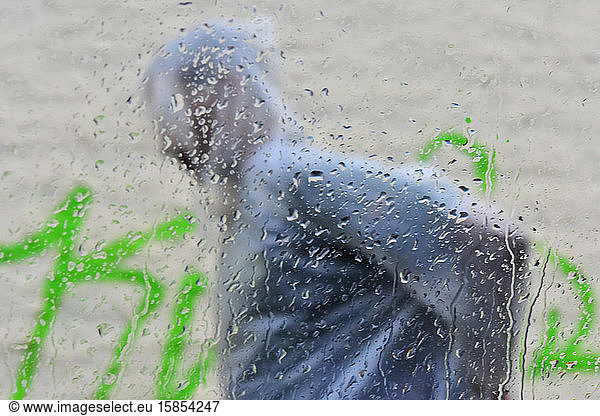 Mann in Regenmantel fährt mit Regentropfen vor einem Auto vorbei