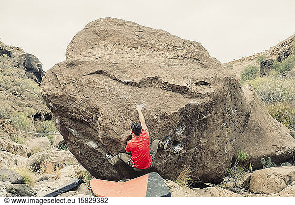 Mann in rotem T-Shirt klettert einen Felsbrocken