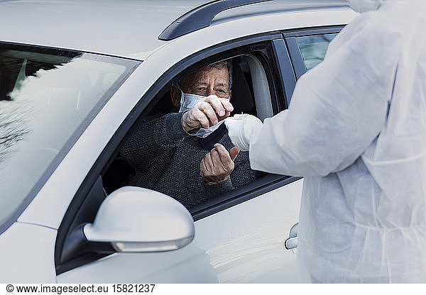 Mann in Schutzkleidung kontrolliert älteren Mann im Auto
