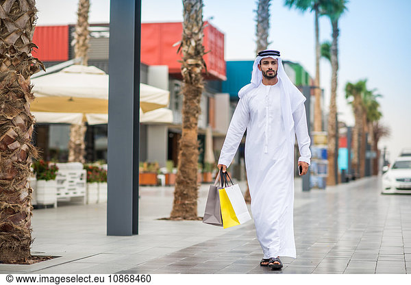 Mann in traditioneller Kleidung aus dem Nahen Osten geht mit Einkaufstaschen durch die Straße  Dubai  Vereinigte Arabische Emirate