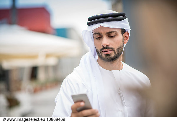 Mann in traditioneller Kleidung aus dem Nahen Osten liest Smartphone-Text  Dubai  Vereinigte Arabische Emirate