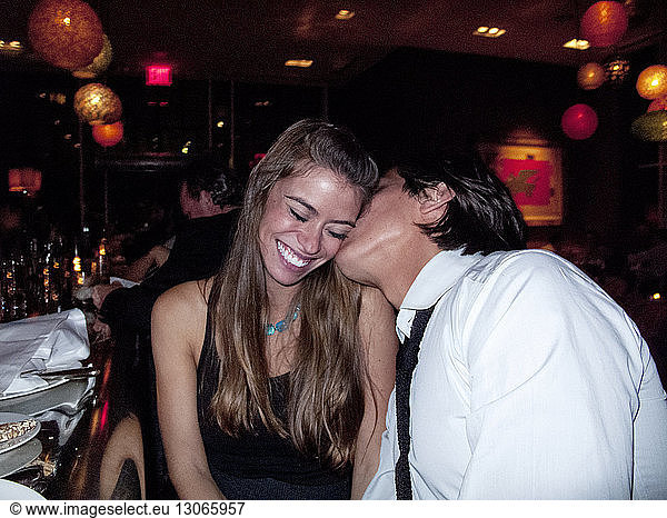 Mann küsst lächelnde Freundin im Restaurant