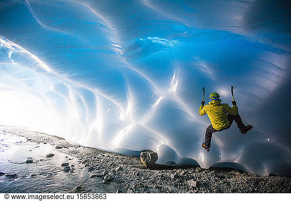 Mann klettert auf Gletschereis in Eishöhle.