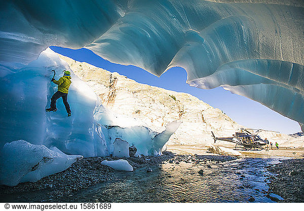 Mann klettert auf Gletschereis neben dem Hubschrauber während einer Abenteuertour.