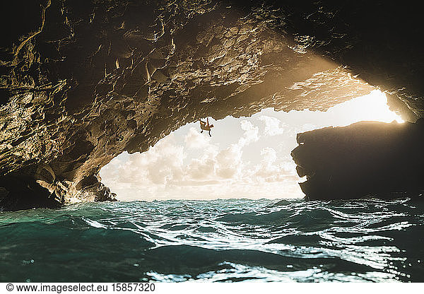 Mann klettert bei Sonnenuntergang in einer vulkanischen Höhle über den Ozean