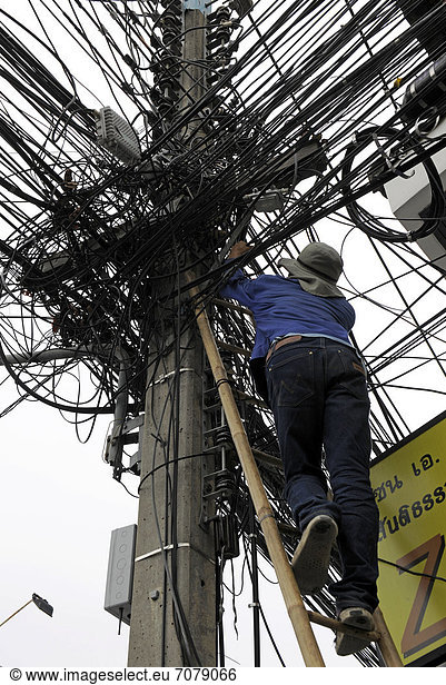 Mann klettert eine Leiter hoch an einem Stromleitungsmasten  Chiang Mai  Thailand  Asien